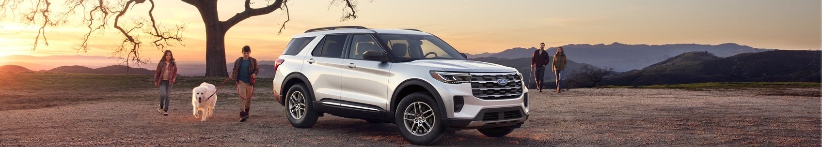 Ford Explorer parked on mountain scenic view with couple and their dog walking towards it